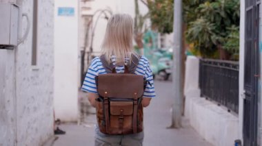 Beyaz tişörtlü, sırt çantalı sarışın bir kadın. Boş caddede yürüyor ve gezmekten, yeni bir yerden ve gezmekten hoşlanıyor. Old Town 'da küçük işlek bir cadde. Grucija, Türkiye