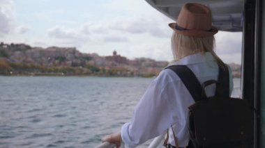 Sırt çantalı, güneş gözlüklü genç bir kadın İstanbul 'da feribotta, boğazında dinleniyor. Beyaz tişörtlü kız gemiye biniyor. Tekne. Dalgalar arka planda. Tekneyle şehri gezmek.