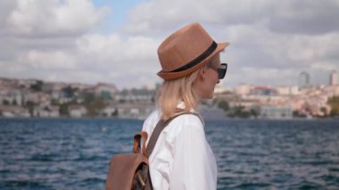 Sırt çantalı, güneş gözlüklü genç bir kadın İstanbul 'da geziniyor, Boğaz' da giden gemileri seyrediyor, gülümseyen turist kız portresi çiziyor. Şehri keşfet ve seyahat et..