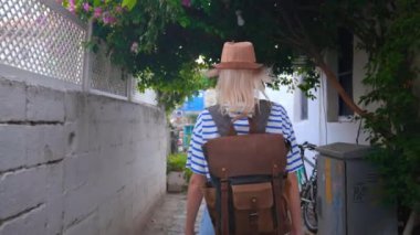 Sırt çantası ve hasır şapkalı kadın turist, Türkiye 'nin Yunanistan, Kıbrıs' ın eski bir kesimindeki boş beyaz caddede yürüyor, tatilinin tadını çıkarıyor, gülüyor, dans ediyor ve kendi etrafında dönüyor..