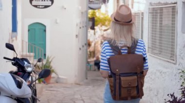 Sırt çantası ve hasır şapkalı kadın turist, Türkiye 'nin Yunanistan, Kıbrıs' ın eski bir kesimindeki boş beyaz caddede yürüyor, tatilinin tadını çıkarıyor, gülüyor, dans ediyor ve kendi etrafında dönüyor..