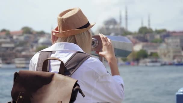 戴着沙龙帽和背包的年轻游客通过装有硬币的双筒望远镜观看城市 乘坐着望远镜从博斯普鲁斯海峡驶过的船只上飞驰而过的年轻而快乐的白人女性 — 图库视频影像