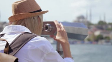 Seyahat: Salon şapkalı ve sırt çantalı genç turist şehre bozuk paralarla dürbünle bakıyor. İstanbul 'da teleskoplu genç ve mutlu bir kadın yolcu Boğaz' dan geçen gemiler ve teknelerle.