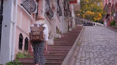 Sırt çantası kırık şapkalı, beyaz tişörtlü, sarışın bir turist. Boş caddede yürüyor, İstanbul 'da Balat Caddesi' nde merdivenleri çıkıyor, gezmekten ve Eski Şehir 'i gezmekten hoşlanıyor.