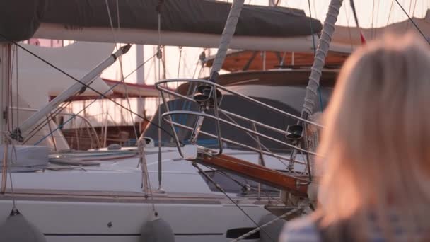 年轻美丽的金发女子 背着太阳镜背包 靠着帆船和游艇在码头上行走 在海上旅行 乘船游览 冒险落日旅行 — 图库视频影像