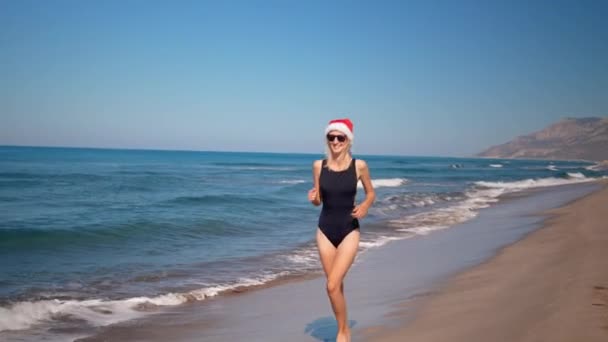 身穿红色兜帽的圣诞老人女人 戴着太阳镜 在海边和山上欢快地跳着舞 海滨圣诞及新年假期的新年及圣诞 — 图库视频影像