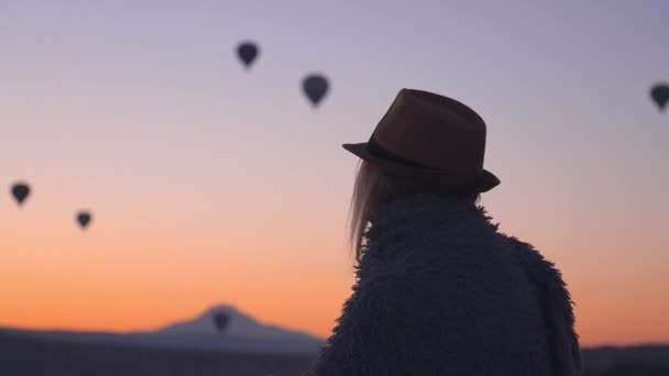 年轻美丽的金发女旅行者裹着毛毯 享受着热气球在土耳其卡帕多西亚的Goreme山上乘坐 黎明时分 在女孩的阳光下 童话故事之旅 — 图库视频影像