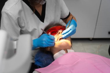 Diş hekimi, aletlerin yardımıyla hastanın dişlerini muayene eder. Dişçi randevusundaki genç kadın..