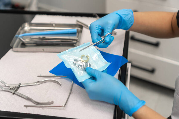 Close-up of the dentist's hand opens a sterile package with clamps. Dental instruments are on the table in the dentist's office.