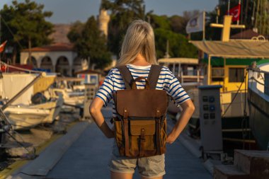 Sırt çantalı genç bir turist gün batımında yat ve teknelerin yakınındaki iskelede duruyor. Arka fotografı Marmaris, Türkiye. Seyahat ve turizm kavramı