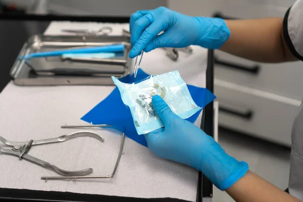 Close-up of the dentist\'s hand opens a sterile package with clamps. Dental instruments are on the table in the dentist\'s office.