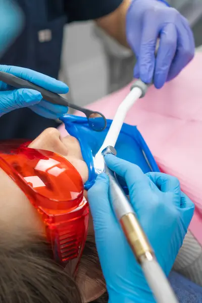 Close-up of a dentist treating a patient\'s teeth with a drill in a dental clinic. Dentist performs dental cleaning, treatment and canal filling. Assistant sterilizes the oral cavity with a saliva pump