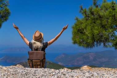 Elleri havada sırt çantalı hevesli bir kadının, inanılmaz güzellikteki dağ ve deniz manzarasına dik bir bakış açısı. Özgürlük ve macera kavramı.