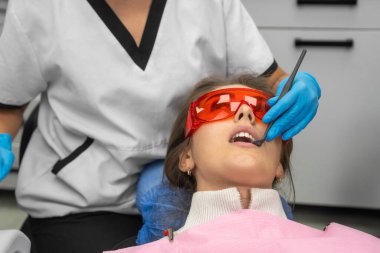 Üniformalı kadın dişçi, tıbbi maske diş kliniğinde bir hastanın dişlerini muayene ediyor. Diş sandalyesinde yatan çekici bir hasta dişçiden diş tedavisi görür..