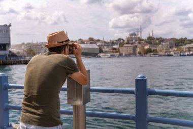 Şapkalı bir turist İstanbul 'daki Galata Köprüsü' nde dürbünle bakıyor. Seyahat ve turizm kavramı. Turistler için gözlem güvertesi