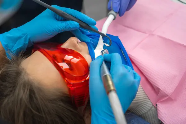 Close-up of a dentist treating a patient\'s teeth with a drill in a dental clinic. Dentist performs dental cleaning, treatment and canal filling. Assistant sterilizes the oral cavity with a saliva pump