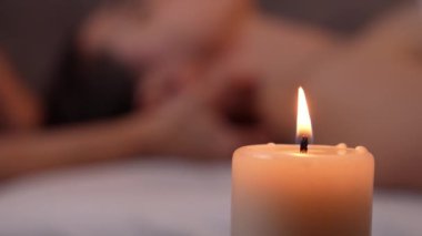 Masör bulanık arka planda kaplıca salonunda kadın vücut masajı yapıyor. Ön planda, aroma mumu yanıyor. Güzellik Tedavisi Konsepti. Sıcaklık ve konfor atmosferleri. Vücut bakımı, güzellik ve sağlık.