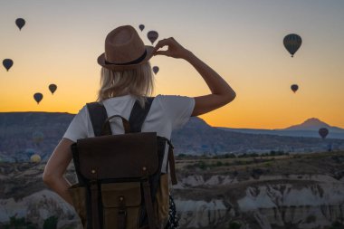 Sırt çantalı genç turist balon manzarası ve Türkiye 'nin Kapadokya kentinde gün doğumunun keyfini çıkarıyor. Dağın tepesinde güzel bir kadın güzel bir manzaranın tadını çıkarıyor..