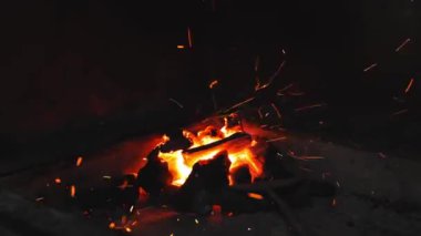 Restoranda kamp ateşinde yemek pişirmek. Aşçı yelpazeyle kömür üflüyor. Koyu arkaplanda yavaş çekimde uçan kıvılcımlar.
