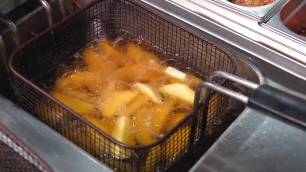 大きなスライスのジャガイモのクローズアップは 深いフライヤーで調理されます ジャガイモはキッチンで深いフライヤーで油で揚げる素朴です — ストック動画
