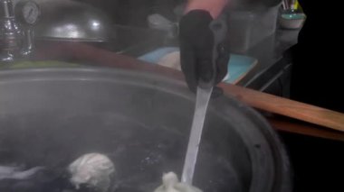 Lokantadaki mutfakta kaynar su ve buharla pişirilmiş khinkali ile büyük kaşık yakın çekim. Aşçı khinkali 'yi kabından çıkarıp tabağa koyar..