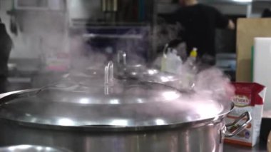 Yemek ya da çorba tencerelerde pişirilir, su ve buhar restoranın mutfağında buharlaşır. Bulanık arkaplan, seçici odaklanma. Tencereler buharlanıyor.