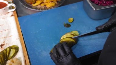 Şef salatalık turşusu hazırlıyor. Salatalık turşusu aşçısı bıçakla parçalara ayırıyor. Mutfak masasında pide ekmeği ve sebze turşusuyla birlikte çalışma ortamı..