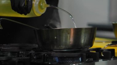 Siyah eldivenli şef yakın planda restoranda tanınmaz halde yemek pişiriyor. Şişeden yiyeceğe sebze yağı ekler.