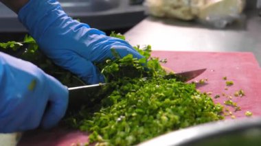 Tahta üzerinde seramik bıçakla taze bitkiler kesiyorum. Mutfaktaki plastik kırmızı kesme tahtasının üzerinde şefin elleriyle kesilmiş taze otlar pişiriyorum..