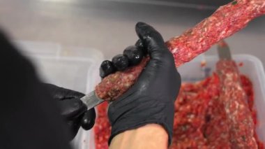 Şef şişe zorla et yapıştırıyor ve onu ticari mutfakta ızgarada lula kebap pişirmek için yapıyor. Siyah eldivenli yakın çekim elleri.