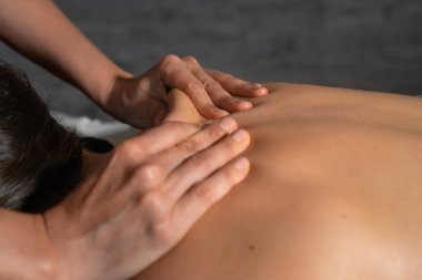 Masözün ellerini yakın plan bir masaj odasında genç bir bayanın sırtına ustalıkla masaj yapıyor..