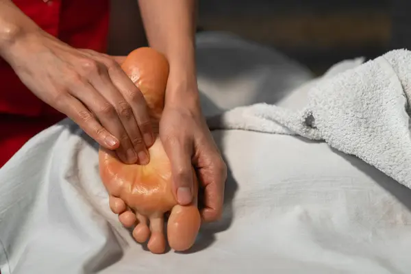 Genç bir bayanın ayak masajı yaparken masörün ellerine yakın çekim. Profesyonel ayak masajı yakın plan..