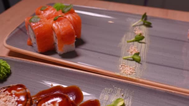 寿司卷 与鲑鱼 奶油奶酪的黑色背景 寿司菜谱日本菜 在它旁边烤了一套寿司卷 上面有芝麻籽和微青菜 — 图库视频影像