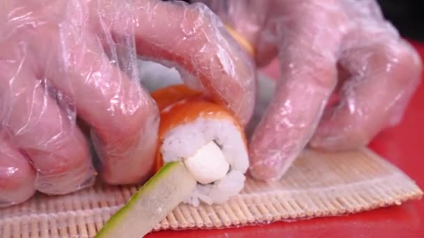 レストランCでフィラデルフィアの寿司を準備するシェフの手のクローズアップは 切削ボードにスライスしたサーモンや赤い魚のスライスを置きます アジア料理が紹介されています — ストック動画