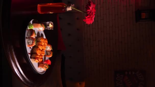 アジアのレストランのテーブルの上の丸いプレートに焼いたロールの寿司セットは 花と燃えるろうそくのインテリアで美しい雰囲気で バーティカルビデオ — ストック動画