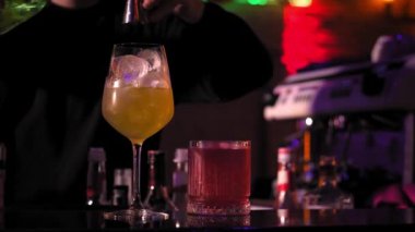 Yakın plan barmen, barın arkasındaki buzlu bardaktan metal karıştırıcıya temiz bir şekilde maden suyu ekliyor..