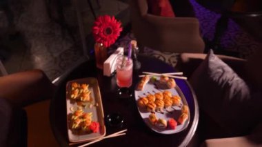 Masada çeşitli lezzetli ağız sulandırıcı suşiler var. Kokteyl, soya sosu, yemek çubukları ve akşam restoranda çiçekli vazo, seçici bir odak noktası..