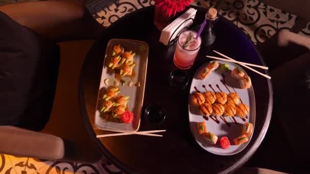 一套美味的 令人垂涎欲滴的寿司卷在桌上 晚上在餐馆里放上鸡尾酒 筷子和一个有花的花瓶 这是有选择的焦点 — 图库视频影像