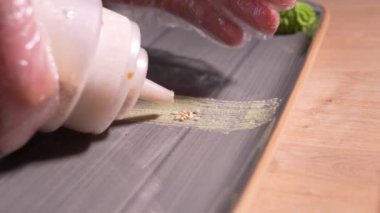 Şef dikdörtgen suşi servis tabağını susam, mikroyeşil ve wasabi ile süslüyor. Mutfakta yemek konsepti, sıkma ve tabak ruloları koymak retsoran ya da bar.