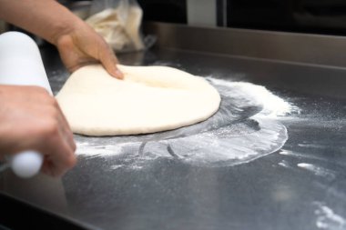 Lokantanın mutfağındaki metal bir masada pizza hamuru pişirip dilimliyor. Pizza hamuru yapıyorum. Seçici odak
