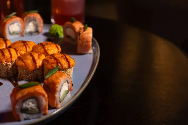 Baked sushi rolls with cheese, fish, sesame seeds and teriyaki sauce on a plate on the table in a restaurant in close-up, copy space