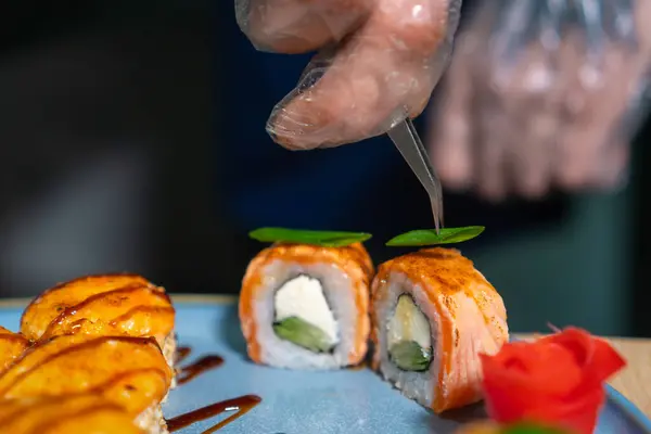 Close-up of the chef decorating baked sushi with small pieces of greens in the kitchen at the restaurant