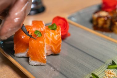 Şef Philadelphia suşisine yeşillik yaprakları koymak için cımbız kullanıyor, yakın plan. Şef restoranda suşi hazırlar. Yiyecek kavramı