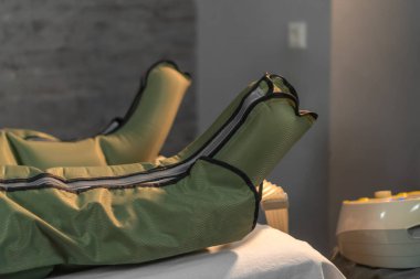 Bir güzellik salonunda tulum içinde pressooterapi prosedürü. Basınç terapisi için tulum giymiş bacakların yakın çekimi. Modern lenfatik drenaj masajı. Sağlık ve güzellik kavramı.