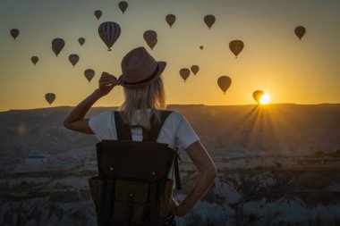 Sırt çantalı genç bayan turist, Türkiye 'nin Kapadokya kentinin güzel bir gündoğumu sırasında aşk vadisinde sıcak hava balonu uçuşlarının inanılmaz manzarasına hayran..