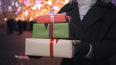 Noel hediye kutularını kadınların elinde kapatın. Noel için hediyeleri olan bir kadın ya da tatil meydanında alışveriş yapan yeni yıl kadını, kadınların elindeki hediye kutularını şehir caddesine yakın çekimde. Doğum günü ya da tatil.