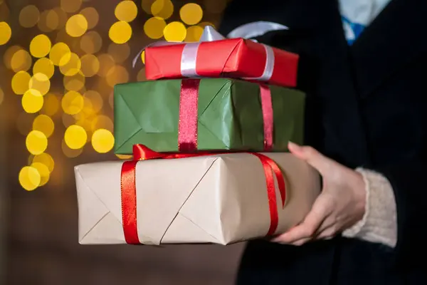 Kadınların elinde Noel hediyesi kutularının yakın çekimi. Sokakta ışıldayan bir çelengin arka planında hediyeleri olan bir kadın. Noel ve Yeni Yıl alışverişi, tatil konsepti. Seçmeli odaklanma