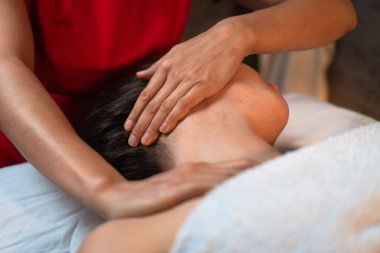 Kırmızı elbiseli masaj terapisti spa ya da güzellik salonunda çalışan genç bir kadına boyun ve omuz masajı yapıyor. Sağlıklı bir vücut kavramı