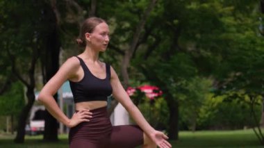Spor giyimli genç bir kadın yemyeşil parkta ısınıyor, antrenmana başlamadan önce bacaklarını esnetmeye özen gösteriyor. Yoga, spor eğitimi..