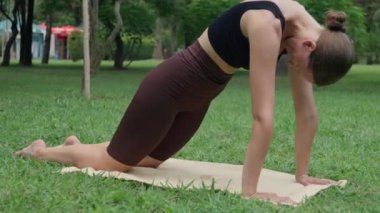 Genç beyaz kadın jimnastik eğitmeni, Mat 'te yoga pozları veriyor yeşil ve güneş ışığıyla dolu yaz parkında. Atletik vücut, sağlıklı yaşam tarzı..